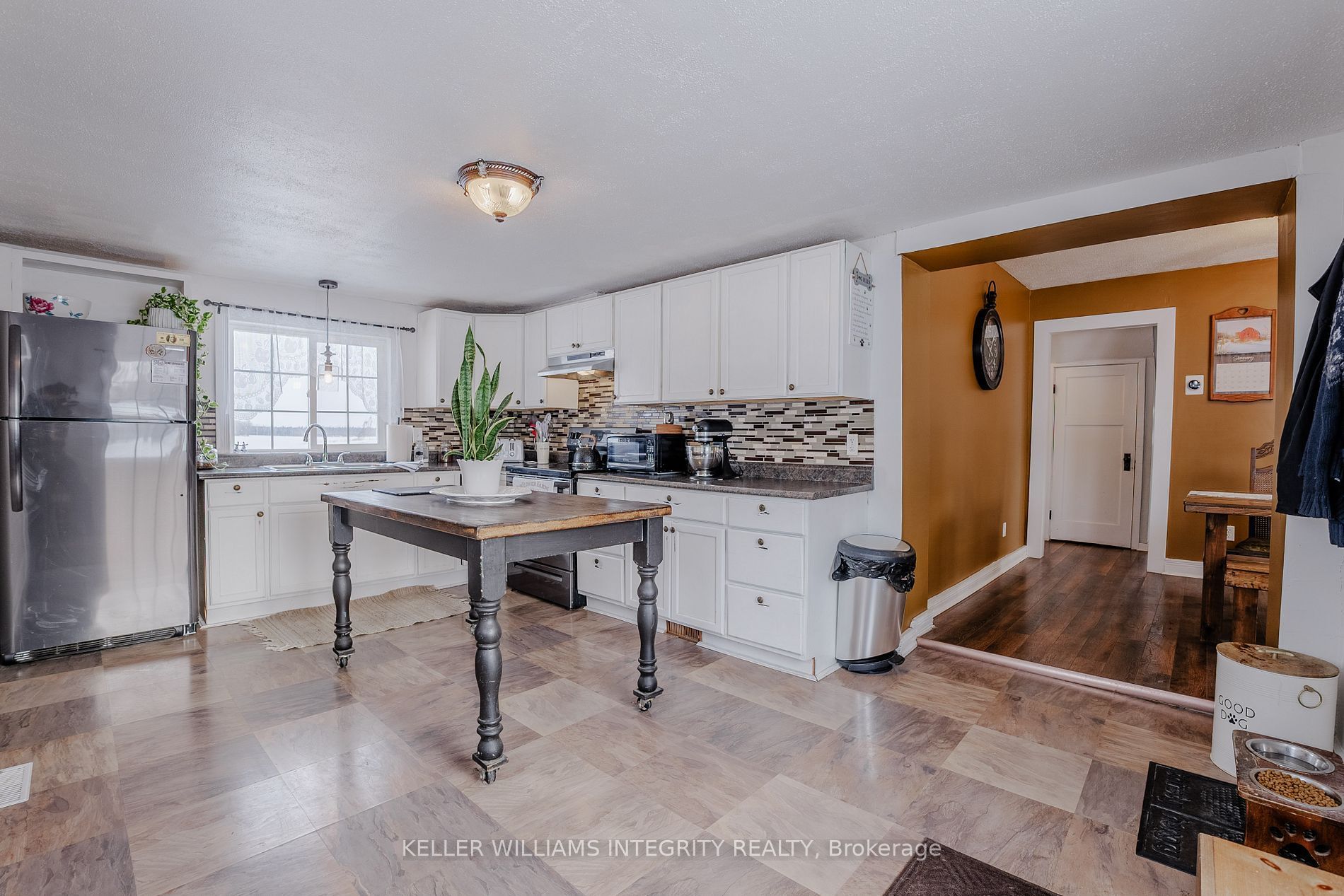 A partial view of a farmhouse-style kitchen with bright white cabinets and a stainless steel refrigerator.